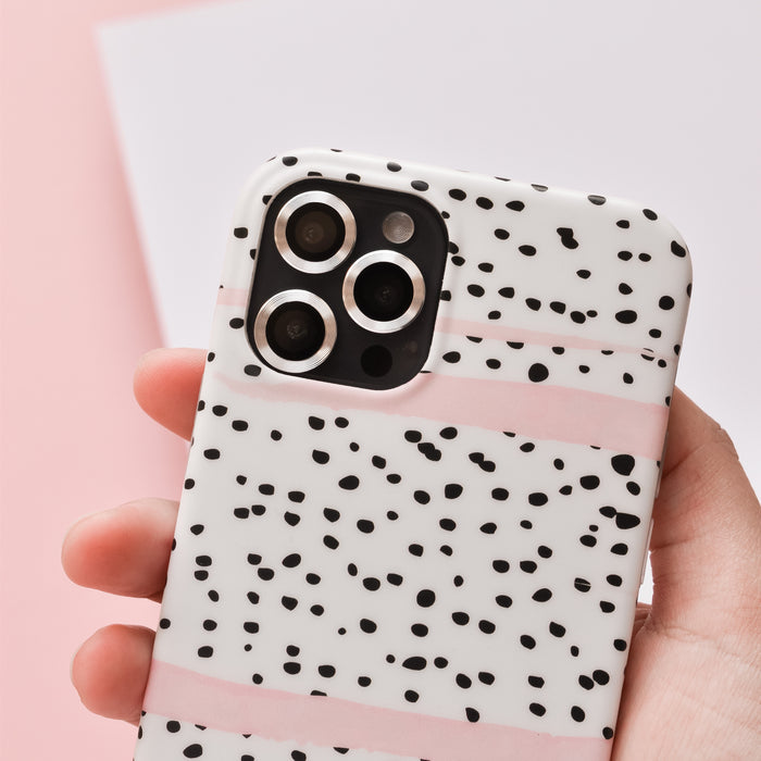 Hand holding a phone with silver Coconut Lane camera lens covers featuring black spots and pink stripes, on pink background.