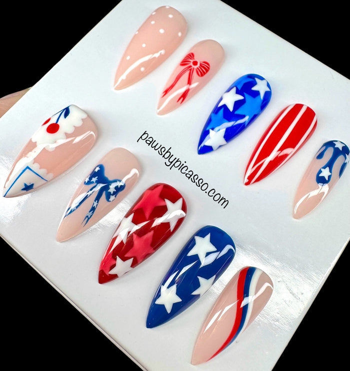 A set of 10 press-on nails displayed on a white card, featuring patriotic red, white, and blue designs with stars and stripes on a black background.