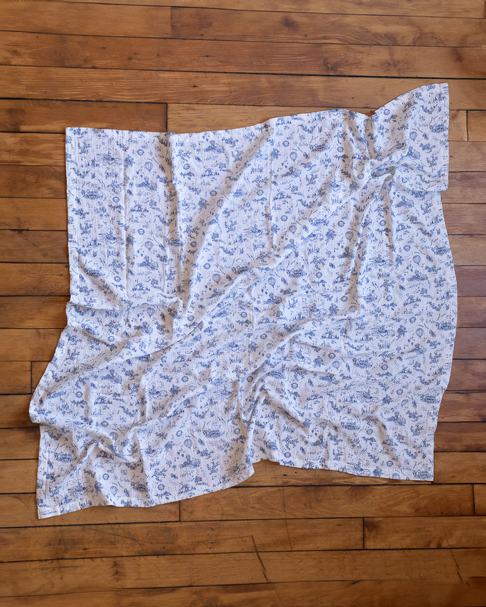 Blue-and-white toile blanket featuring floral motifs, bunnies, butterflies, boats, stars, moons, suns and hot air balloons.