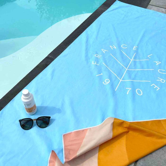 France Laure 1970 beach towel with sunscreen SPF 30 and sunglasses by poolside, ideal for sun protection and summer skincare routines