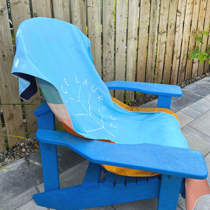 Light blue beach towel with 'France Laure' text and leaf design draped over a blue Adirondack chair outdoors