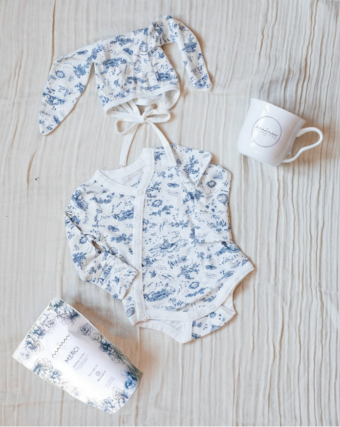 Bundle featuring a blue-and-white toile bodysuit, a matching blue-and-white toile bunny bonnet, Maman coffee, and a Maman hidden bunny mug.