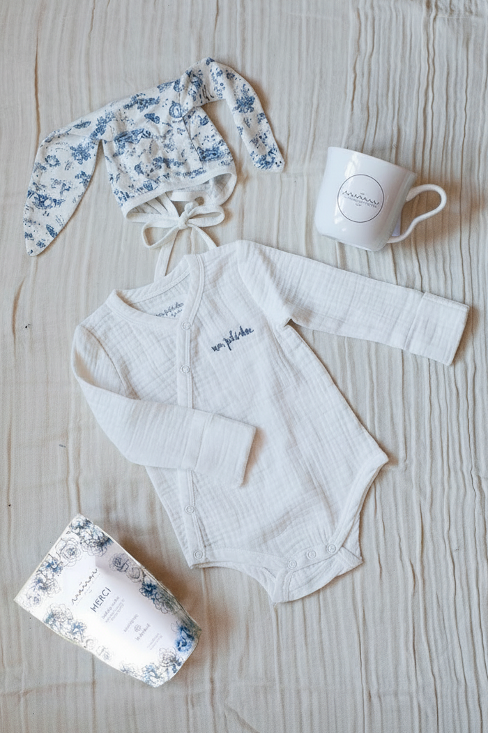 Bundle featuring a white bodysuit with blue “mon petit chou” embroidery, a blue-and-white toile bunny bonnet, Maman coffee, and a Maman hidden bunny mug.