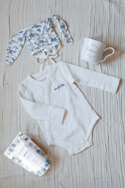 Bundle featuring a white bodysuit with blue “mon petit chou” embroidery, a blue-and-white toile bunny bonnet, Maman coffee, and a Maman hidden bunny mug.