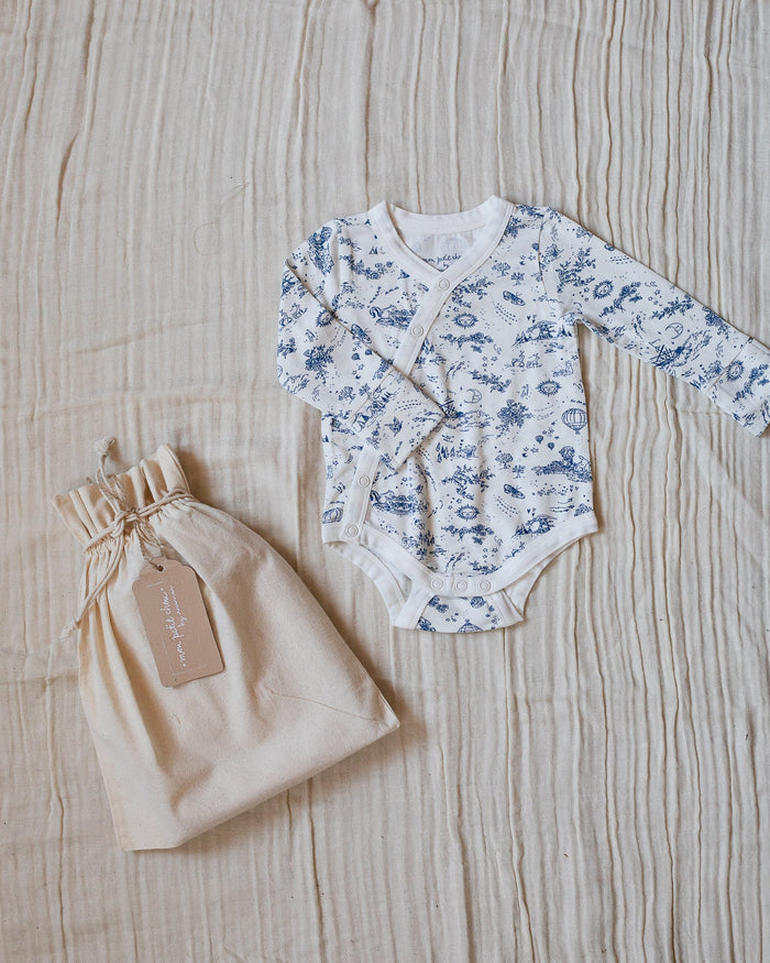 Blue-and-white toile bodysuit with flowers, bunnies, butterflies, hot air balloons, boats, moons, and suns, with its beige canvas bag.