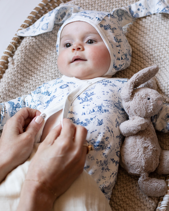Baby wearing a blue and white toile bonnet with bunny ears, and a blue and white toile bodysuit.