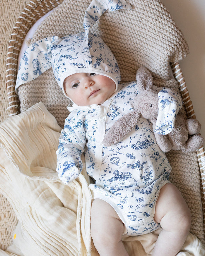 Baby wearing a blue and white toile bonnet with bunny ears, and a blue and white toile bodysuit.