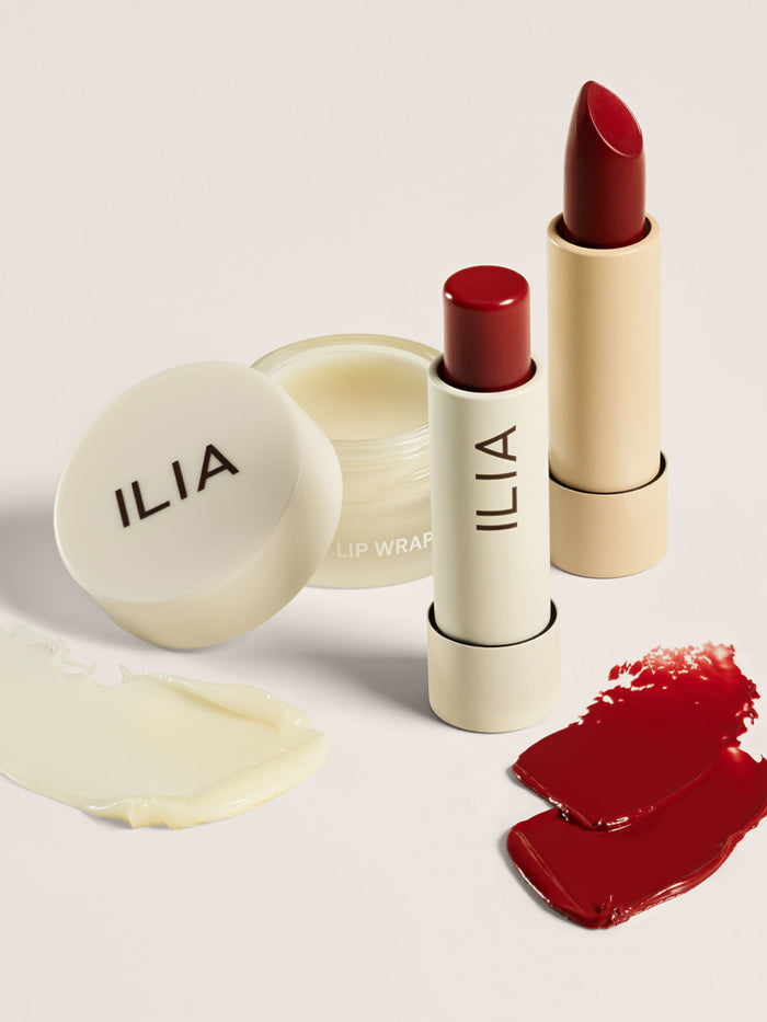 A close-up of ILIA's lip balm, a tinted lip conditioner, and a lipstick, with creamy and red pigment swatches.