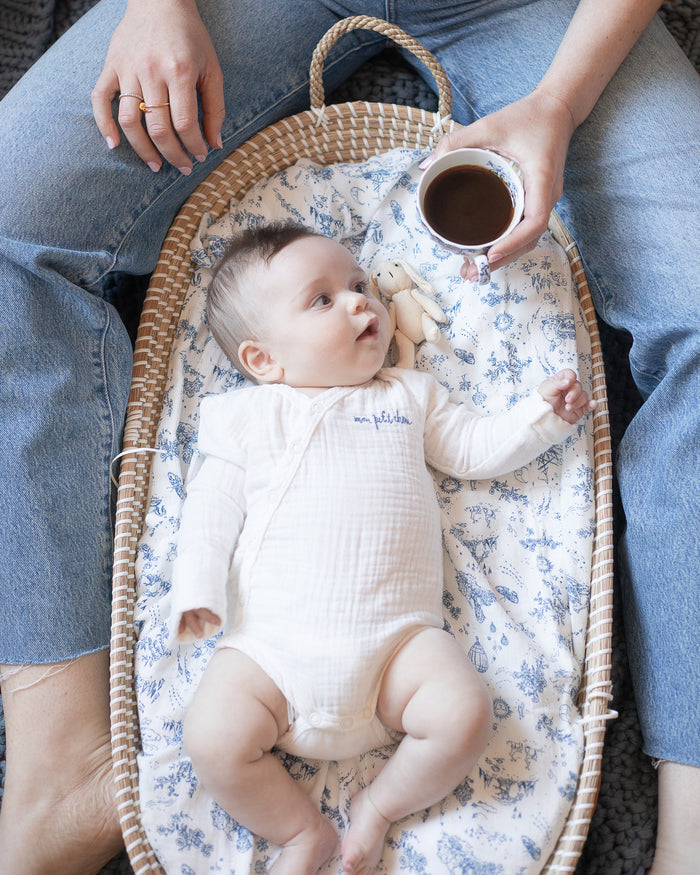 Baby wearing a soft white muslin bodysuit with "mon petit chou" embroidered in blue on the chest, meaning "my little darling" in French.