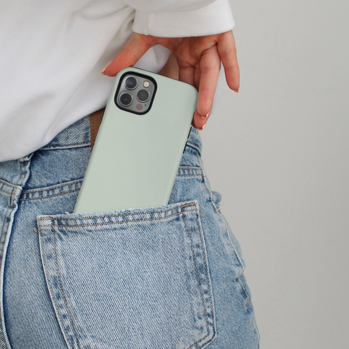 Person in jeans slips a sage green Coconut Lane Tough MagSafe phone case into their pocket, wearing a white top.