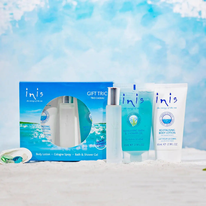 inis Gift Trio set, a blue gift box, a body lotion, a cologne spray, and a shower gel tube, on sand with a blue background