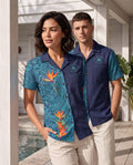 Two models wearing matching short-sleeve camp collar shirts from The Palm Club & Resort. The woman's shirt is teal with a paisley pattern and orange bird of paradise flowers, while the man's shirt is navy blue with a solid front panel and teal patterned sleeves.