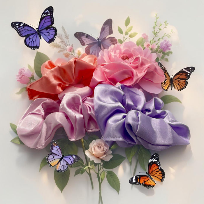 Four satin hair scrunchies in shades of pink, purple, coral, and light lavender, arranged in a bouquet with artificial flowers, green leaves, and four butterflies on a white background.