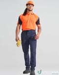 Man in orange flexi work pants with water repellent DWR finish holding yellow gloves