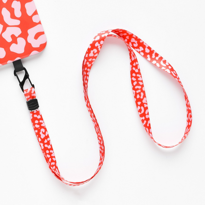 A red Coconut Lane lanyard with a white leopard print pattern is attached to a matching Universal Phone Lanyard Patch Bundle in red and white. The lanyard features a black clasp connecting it to the phone security accessory. The background is a plain white surface.